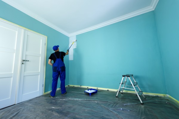 Man in overalls painting blue walls white